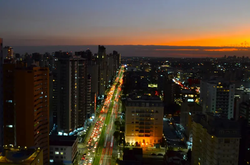 Vista aérea de Curitiba ao entardecer, com prédios e avenidas iluminadas